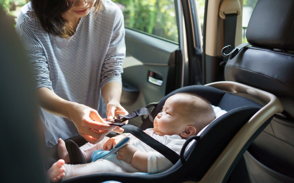 Asian Mother securing her baby in a car seat in the backseat of a car, ensuring safety.