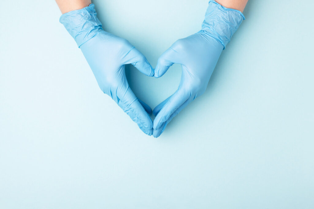 A photo of a doctor's hands in medical gloves in shape of heart on blue background