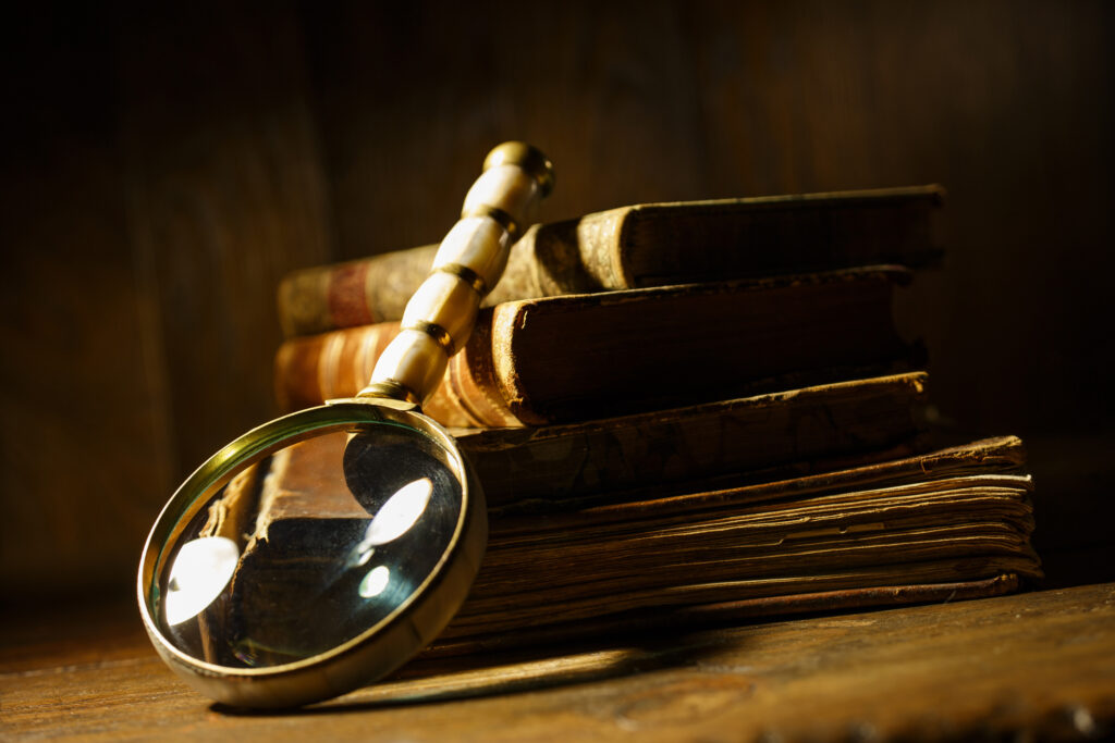 Button to more information on the District's history consisting of a photo of a vintage magnifying glass with antique books. 