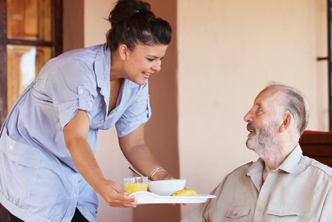 Woman bringing meal to senior man in his home