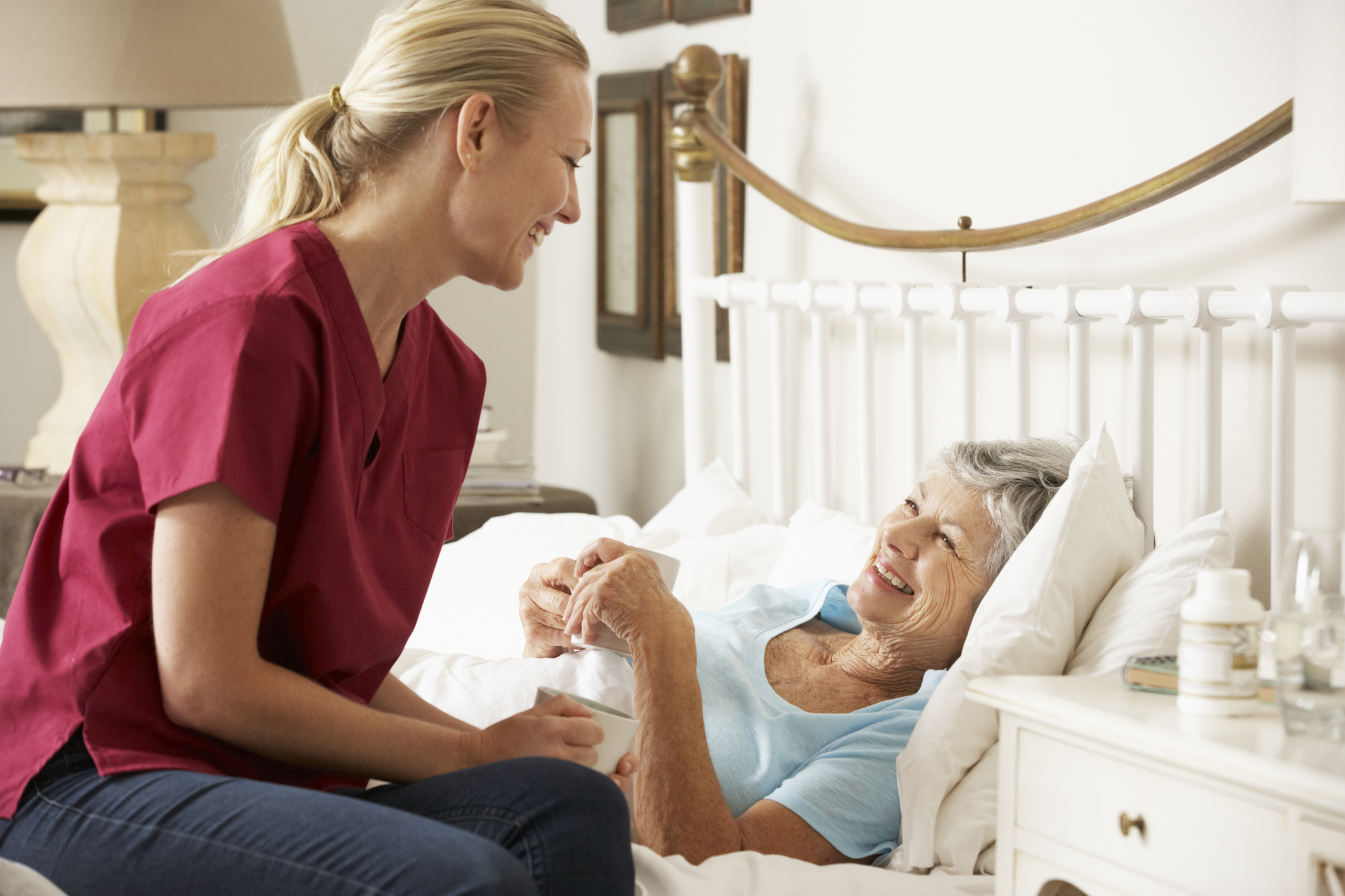 A photo of a visitor talking to a smiling senior patient in a hospital bed